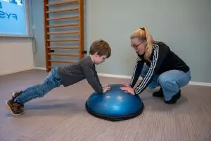 Kinderfysiotherapeut sport met jongen op een bosubal tijdens de kidsgym